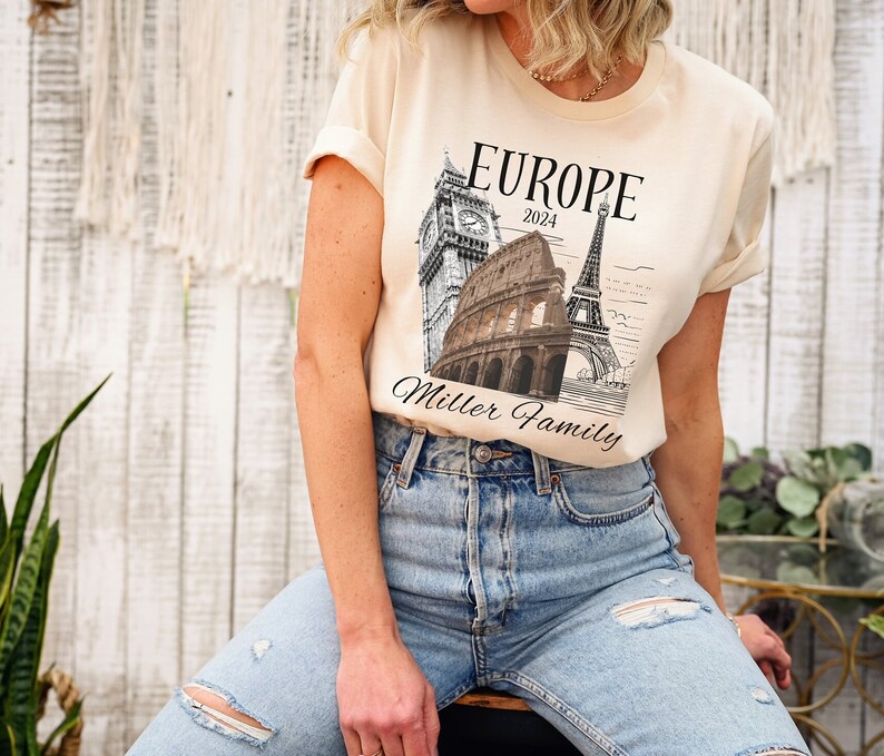 May include: A beige t-shirt with a graphic of the Eiffel Tower, Big Ben, and the Colosseum. The text "Europe 2024 Miller Family" is printed on the shirt.