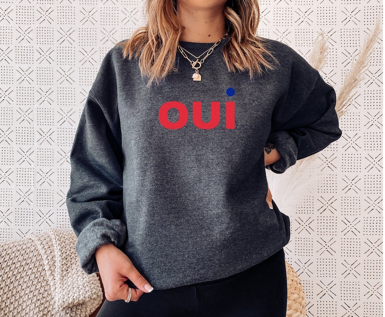 May include: A dark gray sweatshirt with the word "oui" in red letters and a small blue dot above the word.