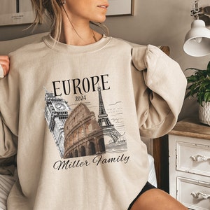 May include: A beige sweatshirt with a graphic print of the Eiffel Tower, Big Ben, and the Colosseum. The text "EUROPE 2024 Miller Family" is printed below the graphic.