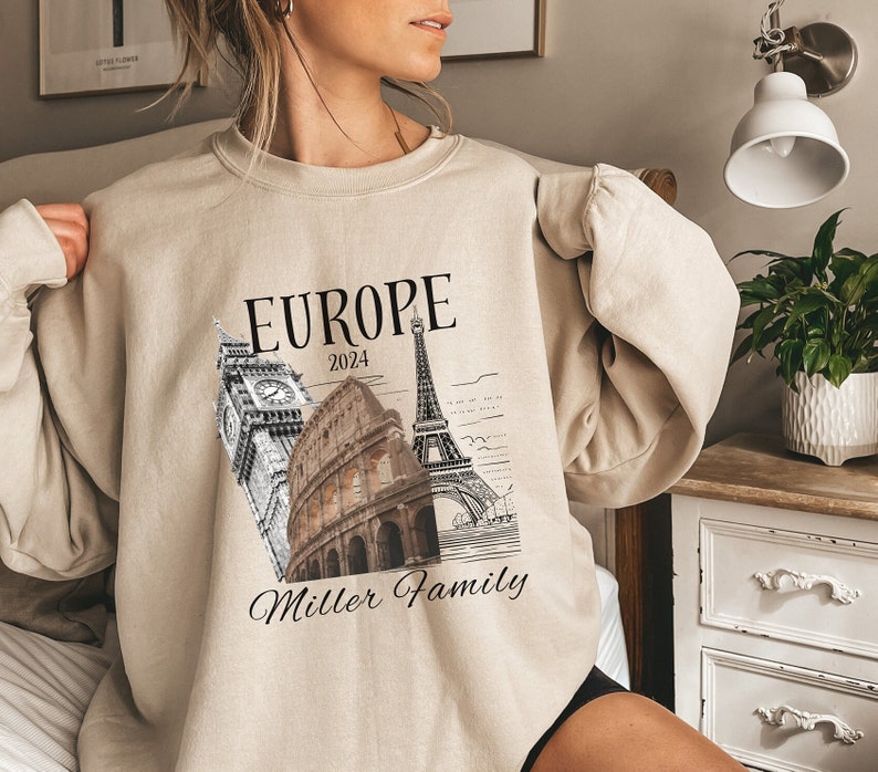 May include: A beige sweatshirt with a graphic print of the Eiffel Tower, Big Ben, and the Colosseum. The text "EUROPE 2024 Miller Family" is printed below the graphic.