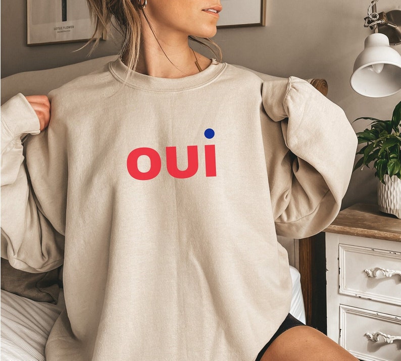 May include: A beige sweatshirt with a red "oui" graphic and a blue dot above the "i".