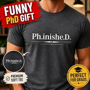 May include: Dark gray t-shirt with the text "Ph.inishe.D." in white, with a line underneath. The shirt also has the text "Funny PhD Gift" in a red banner and a yellow circle that says "Perfect for Grads".