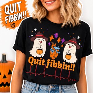 Könnte beinhalten: Schwarzes T-Shirt mit einem Halloween-Design. Das Shirt zeigt zwei Cartoon-Geister mit Hüten und Kürbissen, eine Herzgrafik und den Text "Quit fibbin!!" in Orange. Am unteren Rand befindet sich eine rote EKG-Linie.