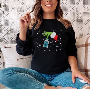 May include: Black sweatshirt with a Grinch-themed design. The graphic includes a green Grinch hand holding a bottle of Propofol, a Santa hat, and snowflakes. The text on the bottle reads "Propofol A Little Bit Is The Best Medicine."