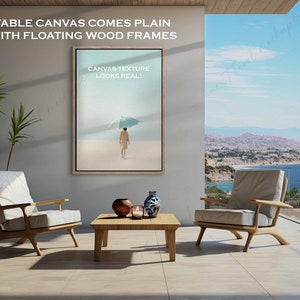 May include: A canvas print of a person walking on a beach with an umbrella. The print is framed in a wooden frame and is hanging on a wall in a living room. The text "CANVAS TEXTURE LOOKS REAL!" is printed on the canvas.