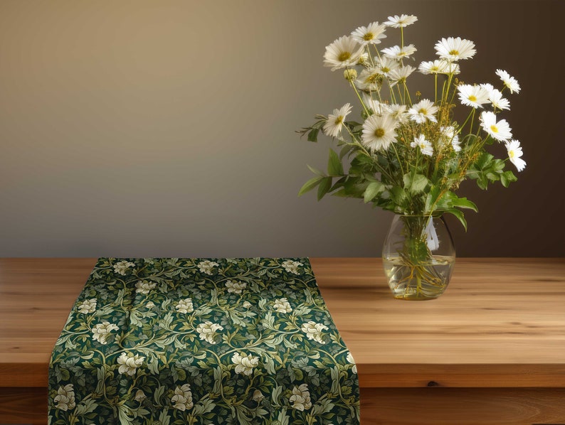 Pu&ograve; includere: Un runner da tavolo floreale verde scuro con fiori bianchi e foglie verdi. Un vaso di margherite bianche &egrave; su un tavolo di legno. Il runner da tavolo &egrave; piegato sul bordo del tavolo.