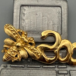 May include: A gold-colored bee pin with the number "30" attached, set against a gray computer-shaped background. The bee has detailed wings and body segments. The number "30" is in a stylized font.