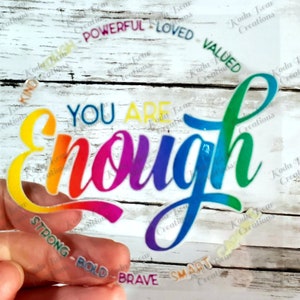 May include: A rainbow-colored vinyl sticker with the text "You Are Enough" in a bold, cursive font. The sticker is surrounded by smaller rainbow-colored stickers with words like "Kind", "Strong", "Powerful", "Loved", "Valued", "Smart", "Bold", and "Brave".