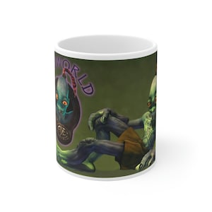 May include: A white ceramic coffee mug with a green background and a cartoon alien character. The alien is green with a large head and is sitting on the mug. The text "World" is written in purple on the mug.