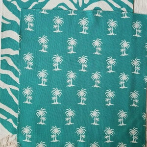 May include: A teal blue fabric with a white palm tree pattern. The fabric has a white fringe border.