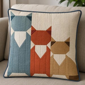 May include: A square throw pillow featuring a quilted patchwork design of three stylized animals in blue, orange, and tan. Each animal is constructed from geometric fabric segments with a cream-colored background and a dark blue piped border.