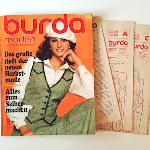 Op de afbeelding: Een vintage Burda Moden magazine uit september 1977, met een vrouw die een groene vest en een wit shirt draagt, met de tekst "Das große Heft der neuen Herbst-mode Alles zum Selber machen 9" op de omslag.
