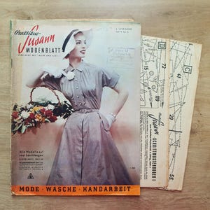 May include: A vintage magazine cover featuring a woman wearing a white hat and a grey dress. The magazine is titled "Praktikus-Jusann MODENBLATT" and has the text "MODE WASCHE HANDARBEIT" at the bottom. The cover also includes a pattern sheet with numbers and lines.