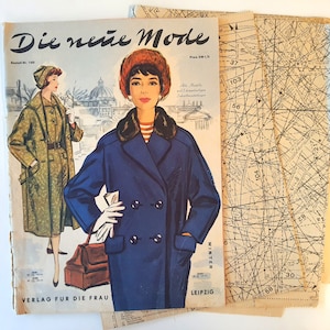 May include: A vintage magazine cover featuring two women wearing coats. The magazine is titled "Die neue Mode" and the text "Winter" is visible on the bottom right corner. The magazine cover is on top of a stack of sewing pattern sheets.