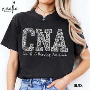 May include: Black t-shirt with a white floral design spelling out "CNA" and the text "Certified Nursing Assistant".