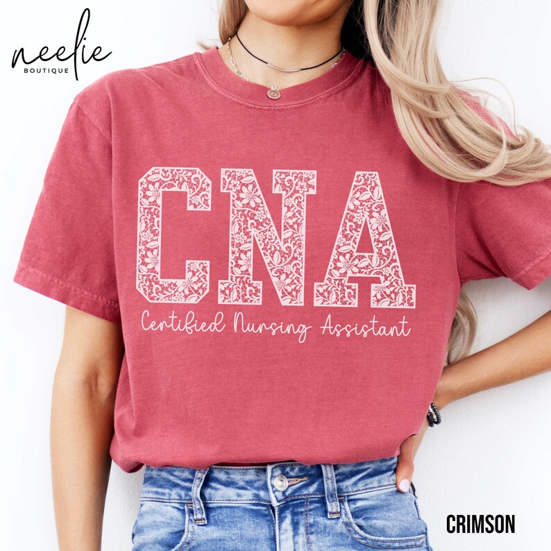 May include: A crimson red t-shirt with a white floral design spelling out "CNA" and the text "Certified Nursing Assistant".