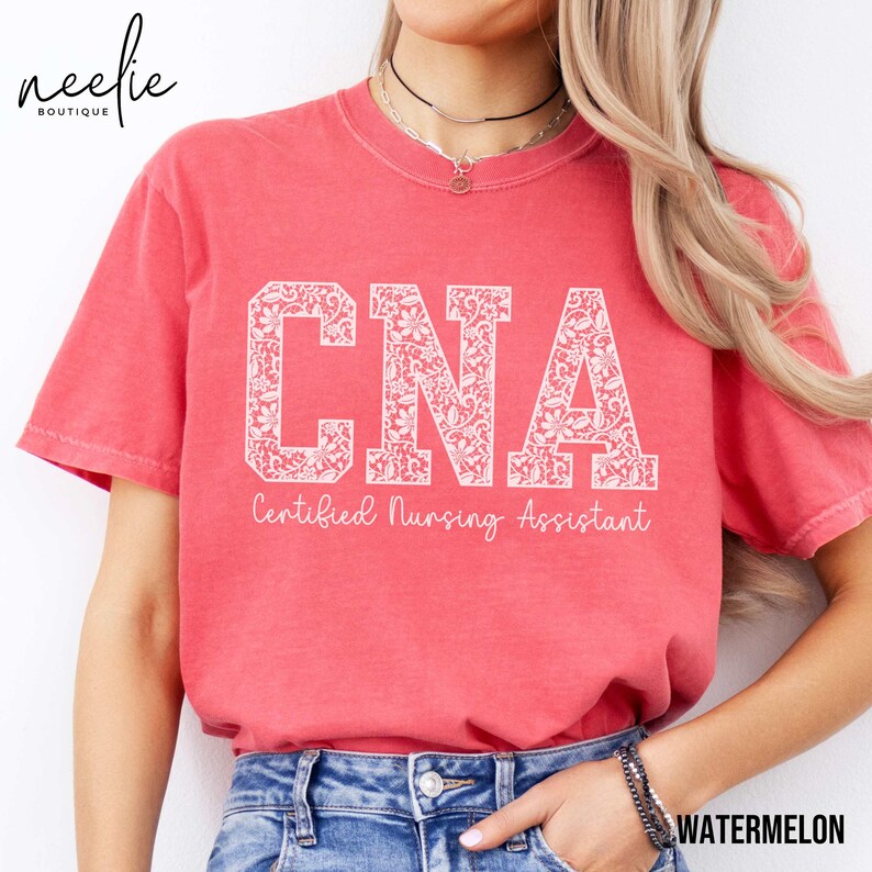 May include: A red t-shirt with a white floral design that spells out "CNA" and the text "Certified Nursing Assistant".