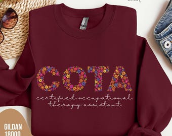 Puede incluir: Sudadera burdeos con cuello redondo con las letras "COTA" llenas de patrones florales coloridos. Debajo, las palabras "certified occupational therapy assistant" están escritas en cursiva. La sudadera es una Gildan 18000.