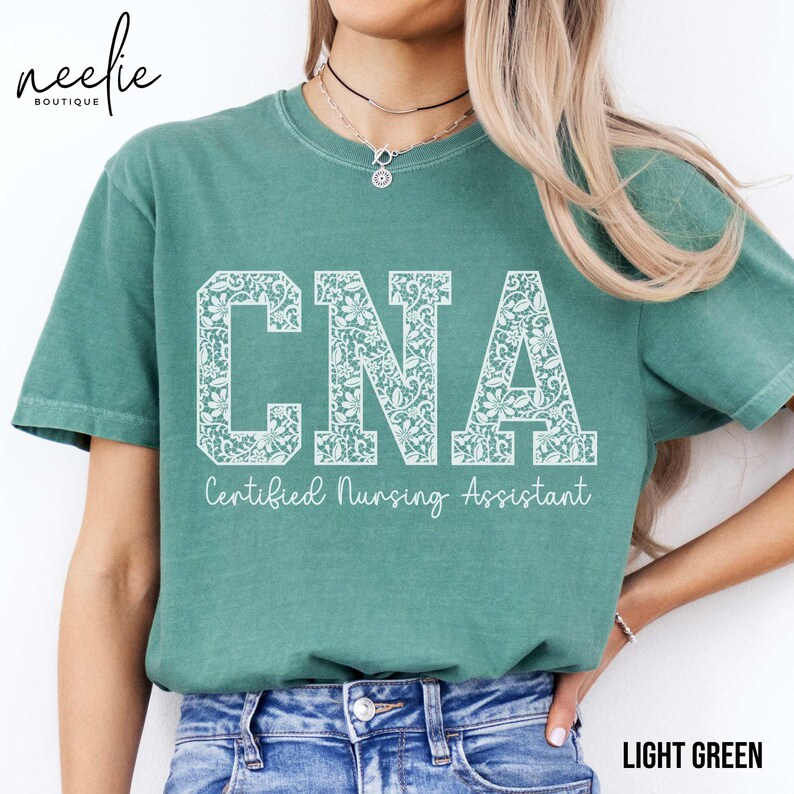 May include: A light green t-shirt with a white lace design that says "CNA Certified Nursing Assistant".