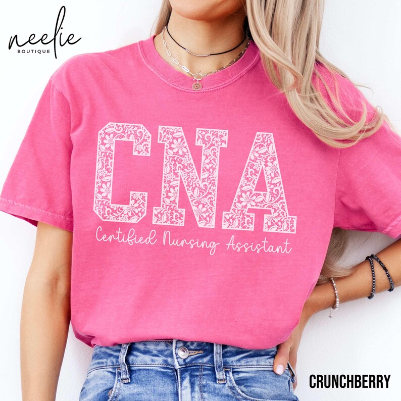 May include: Pink t-shirt with a white lace design that says "CNA Certified Nursing Assistant".