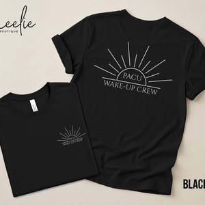 May include: Two black t-shirts with white text and graphics. One shirt has the text "PACU WAKE-UP CREW" on the back, with a sunburst design. The other shirt has the same design on the front, near the chest. The word "BLACK" is at the bottom right.