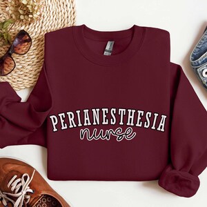 May include: Burgundy sweatshirt with white text that reads "Perianesthesia nurse" in a script font.