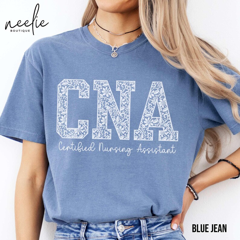 May include: A blue jean t-shirt with a white lace design that says "CNA Certified Nursing Assistant".