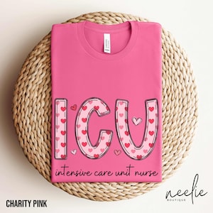 May include: A pink t-shirt with the letters "ICU" in a heart-filled design, with the words "intensive care unit nurse" below. The shirt is folded on a woven, circular surface. The text "Charity Pink" is at the bottom.
