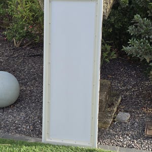 K&ouml;nnte beinhalten: Ein rechteckiges wei&szlig;es Schild mit cremefarbenem Rahmen. Das Schild lehnt an einer Rasenfl&auml;che mit einer Steinstruktur und Gr&uuml;n in der Hintergrund. Das Schild ist leer und bereit zur individuellen Gestaltung.