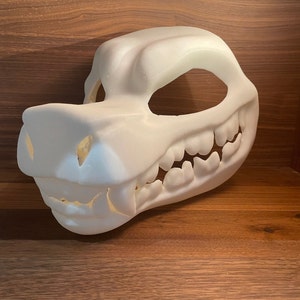 Könnte beinhalten: Weiße, unbemalte, 3D-gedruckte Tiermaske mit einem zahnigen Grinsen. Die Maske besteht aus einem glatten, kunststoffartigen Material und hat einen großen, offenen Mund mit scharfen Zähnen. Die Maske ist so konzipiert, dass sie über dem Gesicht getragen werden kann und Löcher für die Augen hat.