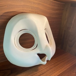 May include: White unpainted owl mask with large eye holes and a beak. The mask is made of a smooth, hard material and is ready for painting.