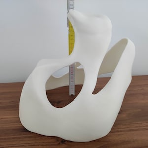 May include: White, abstract, 3D printed sculpture with a large, open, oval-shaped hole. The sculpture is about 15 inches tall.