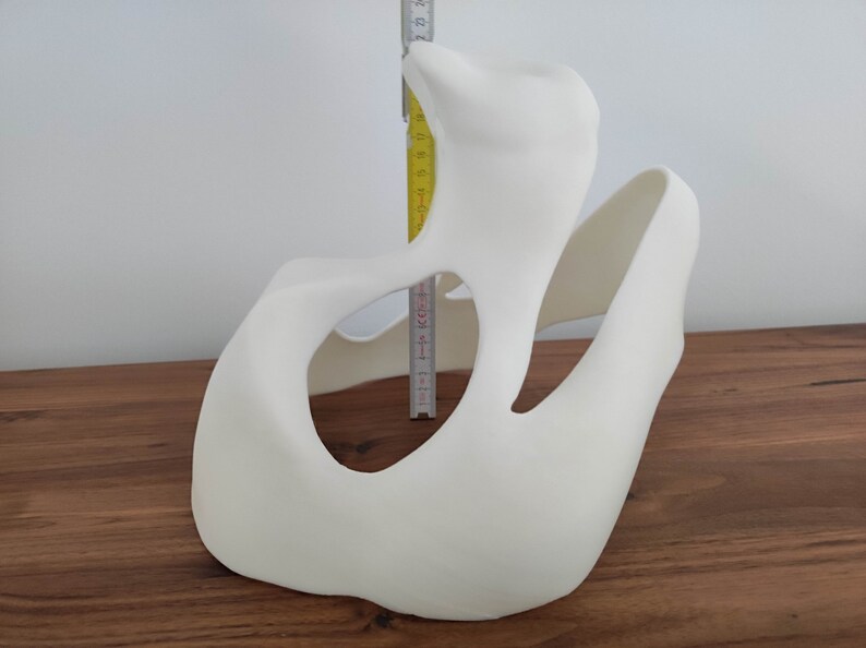 May include: White, abstract, 3D printed sculpture with a large, open, oval-shaped hole. The sculpture is about 15 inches tall.