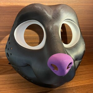 May include: Black furry mask with white eye holes and a purple nose. The mask is made of a smooth, textured material.