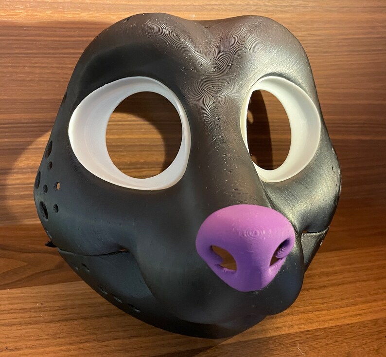 May include: Black furry mask with white eye holes and a purple nose. The mask is made of a smooth, textured material.