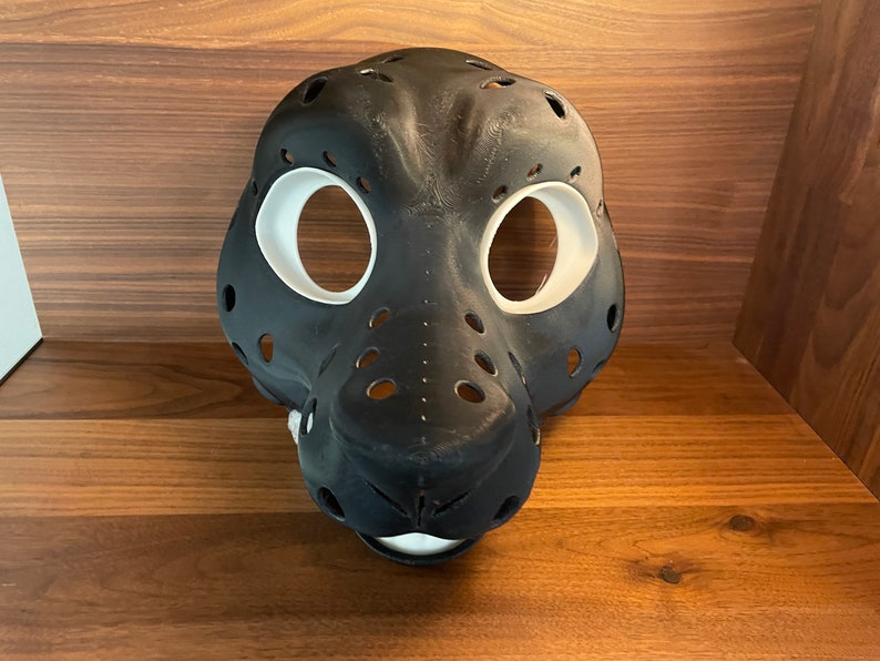May include: A black and white furry animal mask with holes for the eyes and nose. The mask is made of a smooth, hard material and has a realistic look.
