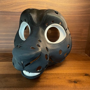 May include: A black and white furry animal mask with holes for the eyes and nose. The mask is made of a smooth, hard material and has a realistic look.
