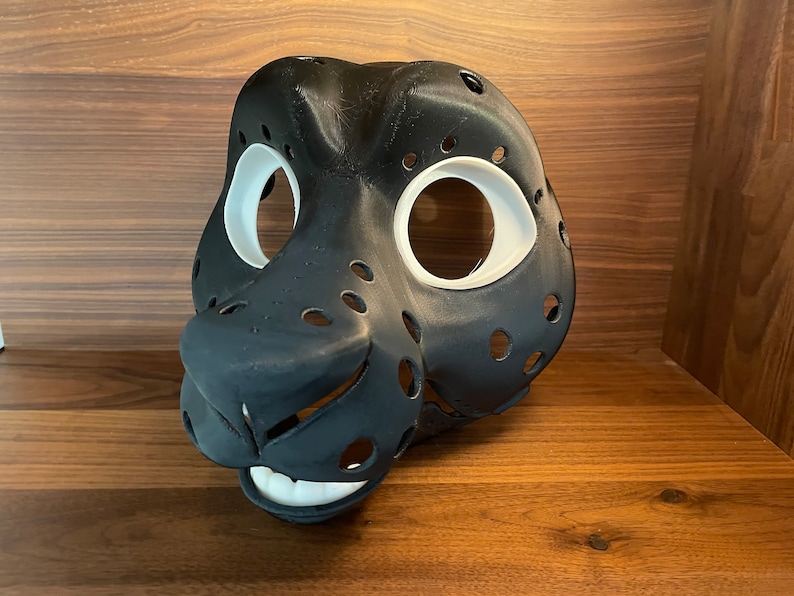 May include: A black and white furry animal mask with holes for the eyes and nose. The mask is made of a smooth, hard material and has a realistic look.