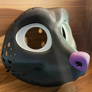 May include: A black furry animal mask with white eye holes and a purple nose. The mask is made of a smooth, textured material and has a detailed design.