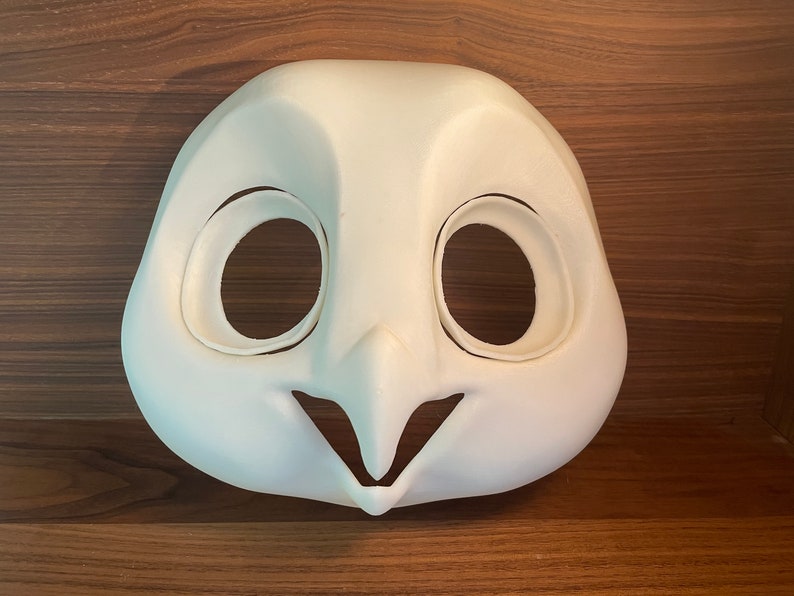 May include: White unfinished owl mask with eye and mouth openings. The mask is made of a smooth, hard material.