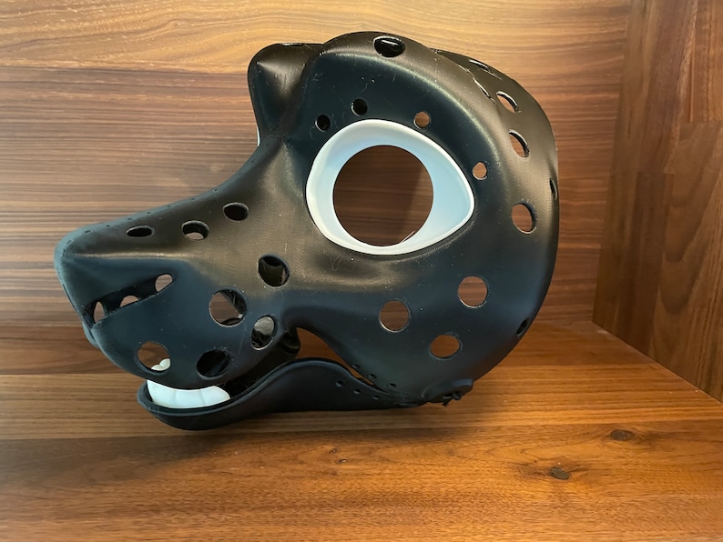 May include: A black furry animal mask with white eye and mouth details. The mask has many small holes throughout.