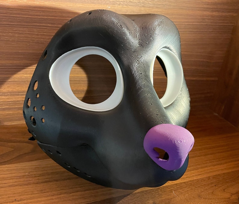May include: A black furry mask with white eye holes and a purple nose. The mask is made of a textured material and has a realistic look.