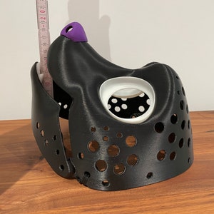 May include: Black 3D printed dog muzzle with a purple nose and white eye holes. The muzzle has a series of small holes throughout.