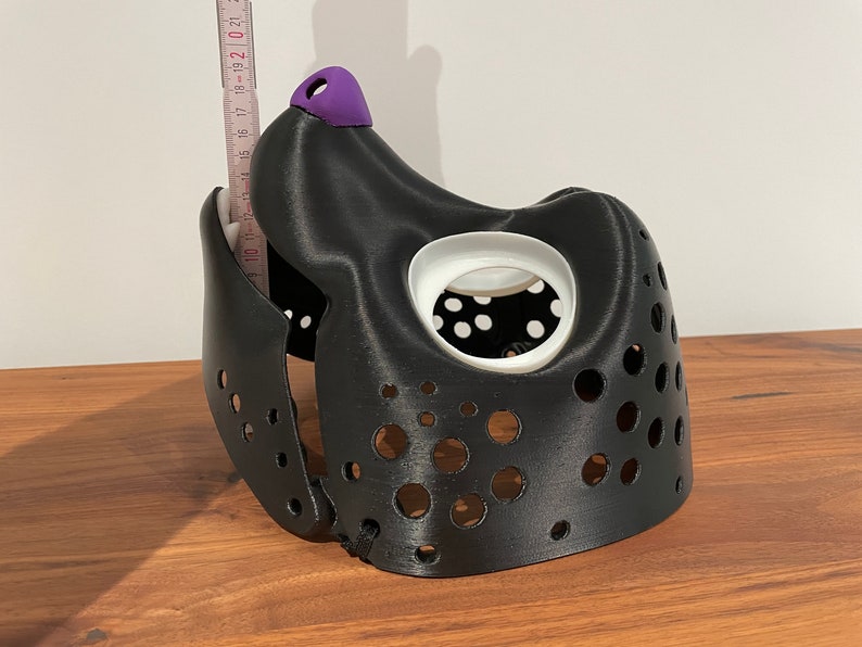 May include: Black 3D printed dog muzzle with a purple nose and white eye holes. The muzzle has a series of small holes throughout.