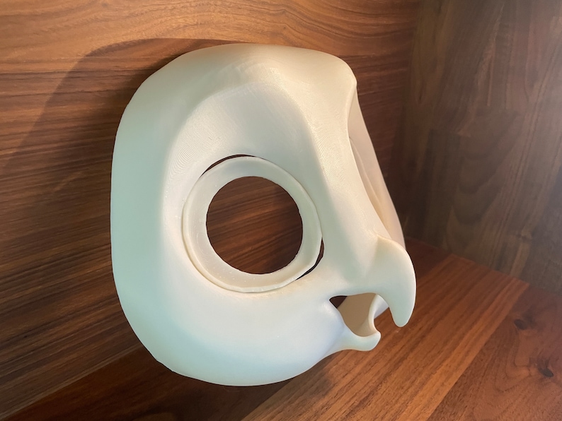 May include: White 3D printed owl mask with a large eye opening and a beak. The mask is made of a smooth, white plastic.