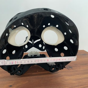May include: Black plastic mask with white interior and holes throughout. The mask is 19 inches wide.