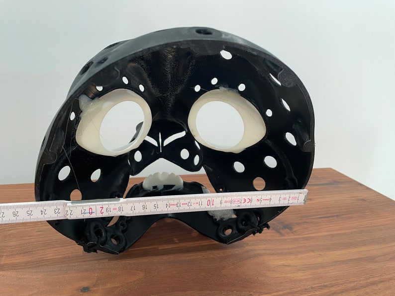 May include: Black plastic mask with white interior and holes throughout. The mask is 19 inches wide.