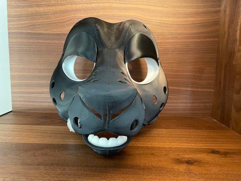 May include: A black and white furry animal mask with white eye holes and a black nose. The mask has a white mouth with teeth.