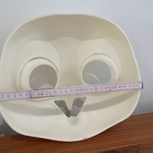 May include: White plastic mask with two eye holes and a mouth hole. The mask is 19 inches wide.