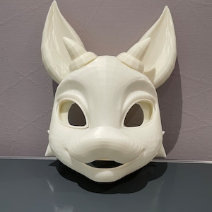 Könnte beinhalten: Weiße, unbemalte Felltiermaske mit großen Ohren und Hörnern. Die Maske hat eine detaillierte Schnauze und offene Augenlöcher.